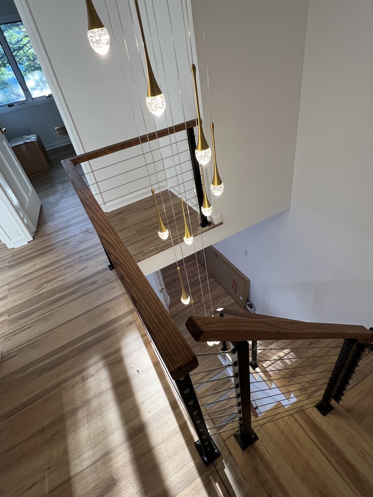 Double-height staircase with black posts, hardwood rails, and cable infill.